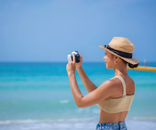 Young woman taking photos by her camera on beach during summer holiday with blue sky background.